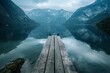   A wooden dock rests atop a tranquil body of water Nearby, forest-covered mountains loom in the distance on a cloudy day