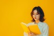 © LidiaLens - Young asian woman reading and enjoying a book in yellow background