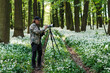 Landscape or wildlife photographer is setting camera on tripod. Man is photographing nature in spring forest