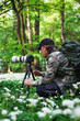 Wildlife photographer. Man with camera on tripod photographing nature in flowering spring woodland
