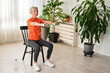 Smiling beautiful senior woman health instructor doing chair exercises with dumbbells