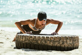 Fototapeta Na drzwi - Woman Doing Push Ups on Tire on Beach