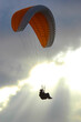 A Paraglider soars into the clouds and the sun behind him causes the person to be a silhouette. 