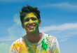 A young man with green and yellow Holi color on face.