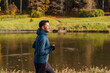 A tranquil jogger in a teal jacket reflects on his run beside a still, reflective lake, amidst the warmth of a golden hour.