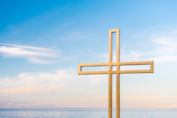 Golden cross against a background of blue sky with clouds. A minimalistic view of a gold-colored cross against the sky.