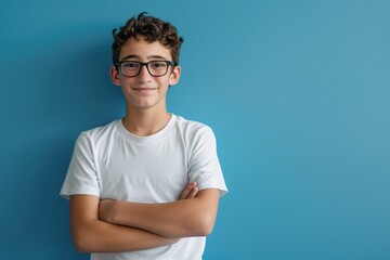 Portrait of a smiling teenage boy wearing eyeglasses, arms crossed, isolated on a blue background