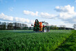 Pflanzenschutz im Ackerbau - roter Traktor mit Feldspritze im Getreidefeld, Heckansicht.