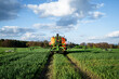 Pflanzenschutz im Ackerbau - roter Traktor mit Feldspritze im Getreidefeld, Heckansicht.