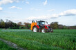 Pflanzenschutz im Ackerbau - roter Traktor mit Feldspritze im Getreidefeld, Frontansicht.