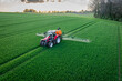 Pflanzenschutz im Ackerbau - roter Traktor mit Feldspritze im jungen Getreidebestand, Luftaufnahme.