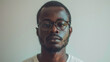 © neatlynatly - African male in eyeglasses and white t-shirt against a plain background, looking at the camera.