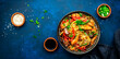 Hot stir fry egg noodles with turkey, paprika, mushrooms, chives and sesame seeds with ginger, garlic and soy sauce. Asian cuisine dish. Blue table background, top view banner