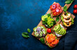 Avocado toasts with salmon, shrimp, vegetables, spinach, capers and cream cheese, served on wooden board, blue table background, top view