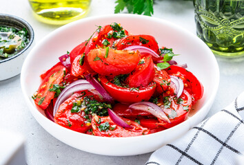 Wall Mural - Summer juicy tomato salad with parsley dill garlic and olive oil dressing and red onion, white table background, top view