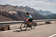 Woman cyclist wearing cycling kit and helmet riding on the road on a gravel bike. Empty mountain road. Sports motivation image. Coll de Rates pass in Spain. Epic mountain view.