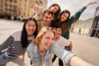 © CarlosBarquero - A group of young people is happily posing for a selfie together while traveling. They are smiling and making gestures of fun and leisure under the clear sky, sharing a moment of recreation and joy