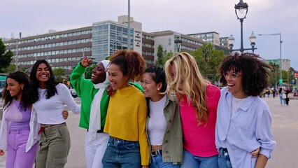 Wall Mural - Multi ethnic group of joyful beautiful women having fun together outdoors. Diverse female friends hugging each other while walking at city street. Friendship and female community concept. 