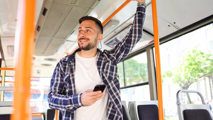 Young man riding in a bus and sending message on smartphone