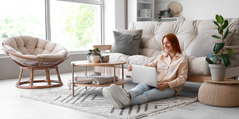 Wall Mural - Young woman with laptop sitting on carpet in living room