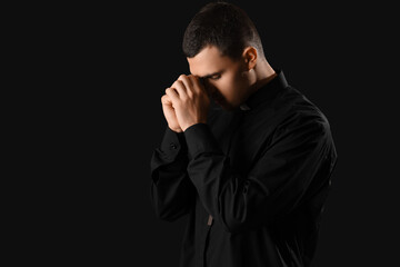 Wall Mural - Young priest praying on dark background