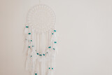Fototapeta Lawenda - Dream Catcher with white feathers and blue beads on a beige wall.Wicker talisman protects against bad dreams. Decoration for home and room. Macrame wall decoration 