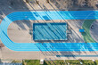 Aerial view of blue running track and multi-sport court in public park. Used to practice football, basketball jogging. Top view. Sunny day. Sunset. Drone photo.