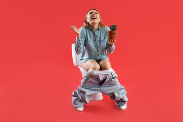 Poster - Mature woman with cactus sitting on toilet bowl against red background. Hemorrhoids concept