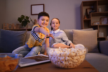 Wall Mural - Little children with popcorn watching TV on sofa at home in evening