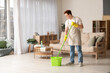 Handsome young man mopping floor in living room