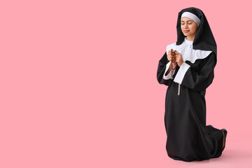 Young nun with beads praying on pink background