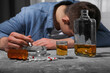 Alcohol and drug addiction. Man with smoldering cigarettes, whiskey and pills at grey textured table, selective focus