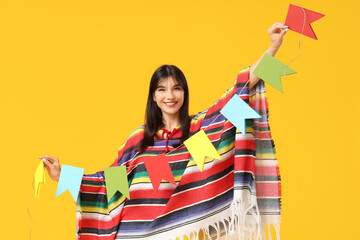 Young woman in colorful poncho with bunting on yellow background. Cinco de Mayo celebration