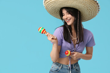 Young woman with sombrero and maracas on blue background. Cinco de Mayo celebration