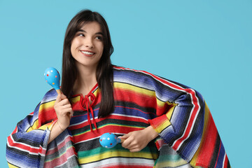 Young woman in colorful poncho with maracas on blue background. Cinco de Mayo celebration