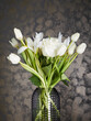 White flowers in a transparent, ribbed vase, with stones lying on a dull gray background.