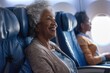 © evgenia_lo - Joyful African American senior woman smiling on an airplane, with another passenger in the background.