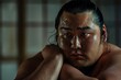 Intense portrait of an Asian sumo wrestler, glistening with sweat and deep in thought.