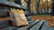A crumpled fast food bag rests on a park bench, fries jutting out, tempting hungry park-goers with their aroma