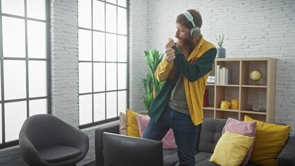 Wall Mural - Bearded young man in casual attire playfully dances in a modern interior while wearing headphones.