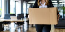 Focused Woman Carrying A Large Cardboard Box Through A Blurred Office Setting, Possibly Signaling A Job Change Or Relocation.