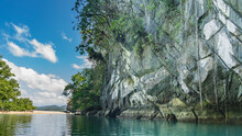Sheer Karst Cliffs Rise Above The Emerald Calm River. Green Vegetation On Steep Slopes. Glare On The Water. Clouds In The Blue Sky. Philippines. Palawan. Puerto  Princesa. An Underground River.