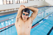 Caucasian young male swimmer stretching before swimming indoors, pool in background