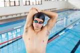 Fototapeta  - Caucasian young male swimmer stretching before swimming indoors, pool in background