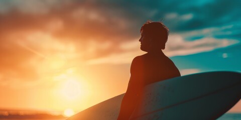 Wall Mural - Backlit surfer holding a board, gazing at the ocean under a vibrant sunset sky.