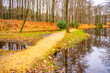 A serene path curves along the lakeside amid colorful autumn leaves in Rhododendron Park, Kromlau, Germany.