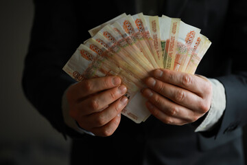Wall Mural - a man in an expensive suit holds a lot of money in his hand, Russian rubles, bills of five thousand rubles
