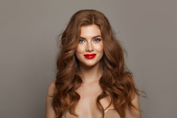 Wall Mural - Young fashionable redhead woman with long wavy hair and make-up. Studio headshot portrait of fashion model lady with red colorful shine lipstick. Haircare, skin care and coloration concept