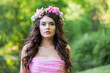 Portrait of healthy woman with makeup and long wavy dark brown hairstyle with flowers on head in spring park outdoor