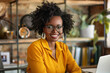 © Moritz - Happy African American Businesswoman Working from Home. Portrait of Young Female Entrepreneur in Yellow Jumper and Glasses Smiling at Desk with Laptop, Remote Work Concept.